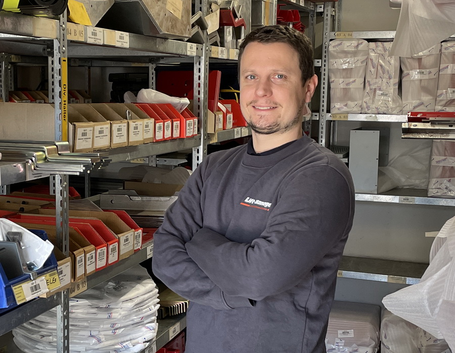 mann vor lager regalen mit verschraenkten armen